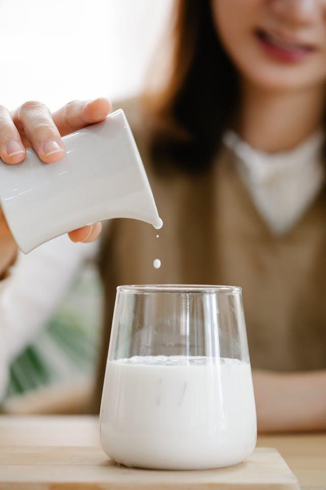 Jeune femme en arrière-plan flou qui tient un récipient blanc avec goutte versée dans verre de lait