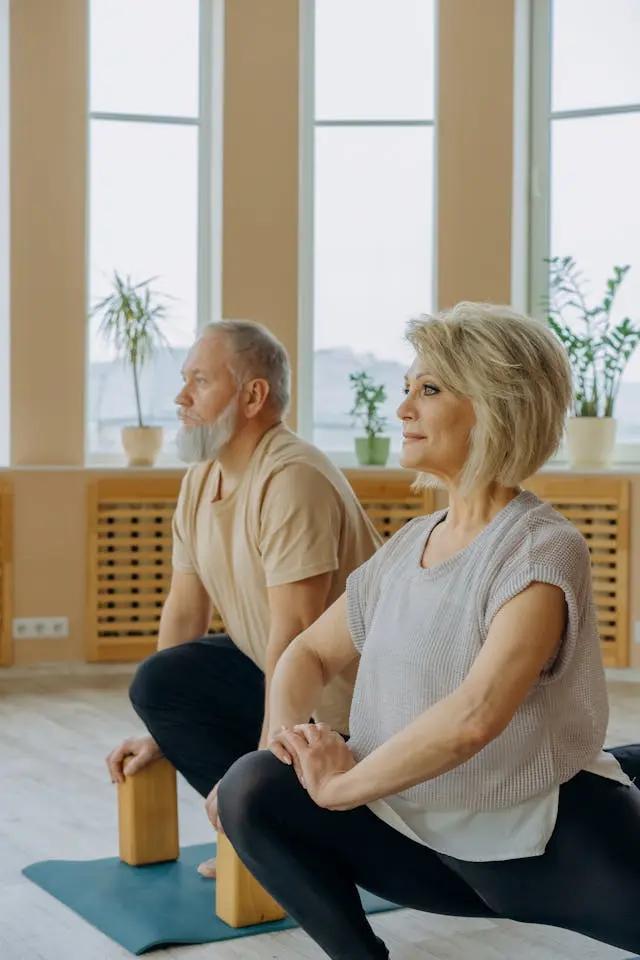 Couple de seniors de profil pratiquant du pilates une jambe étirée à l'arrière et l'autre fléchie devant